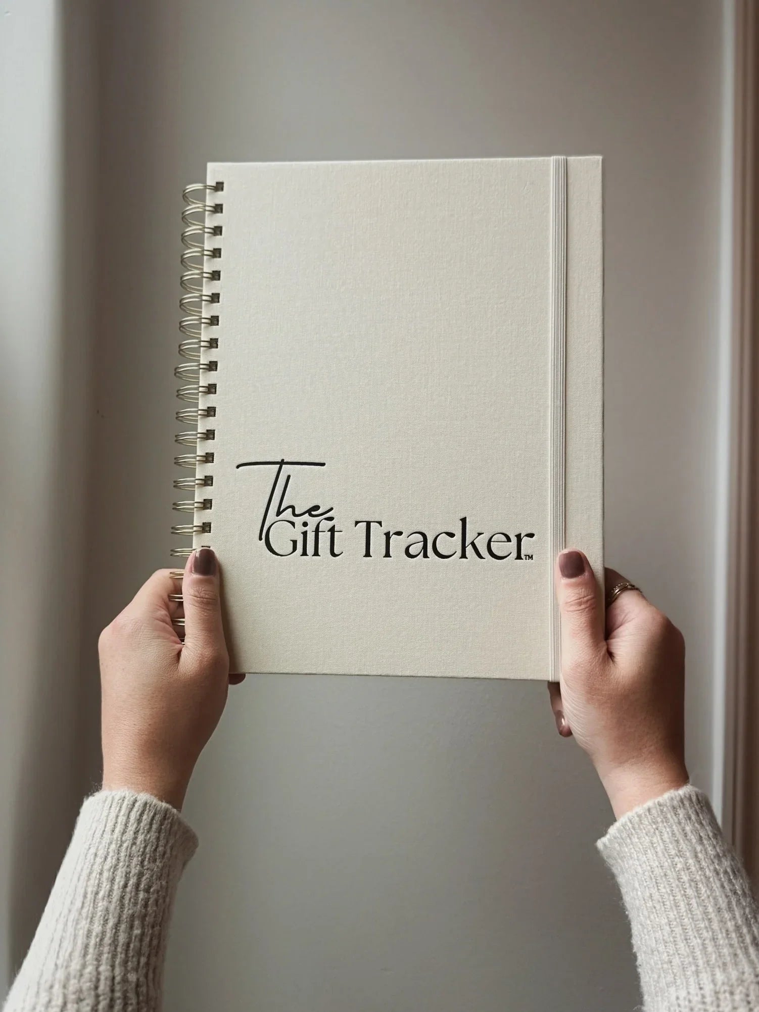 Notebook titled 'The Gift Tracker' held by hands against a neutral background